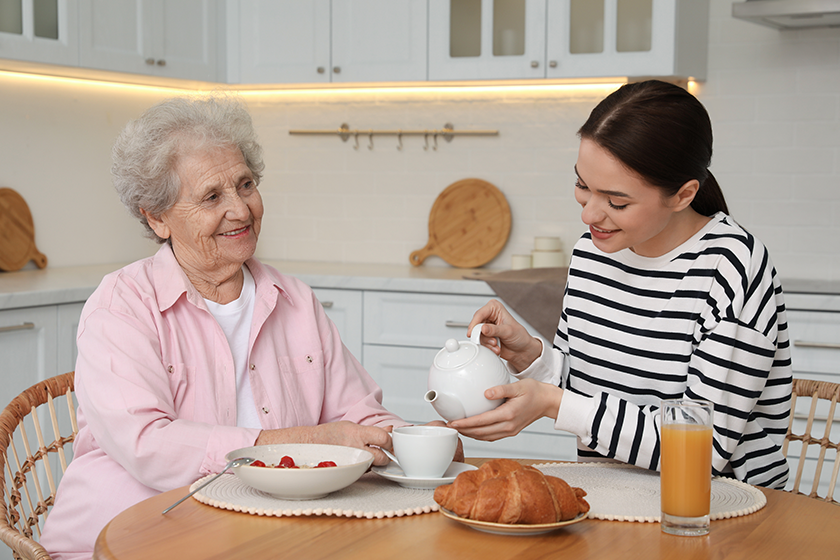 Young caregiver serving breakfast for senior woman 